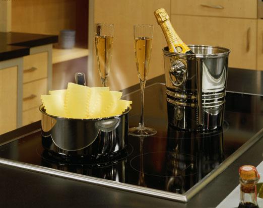 Champagne bottle and glasses on cooktop surface while pasta cooks on another element